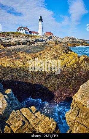Felsen und Meereswellen in der Nähe des weißen Leuchtturms in Maine Stockfoto