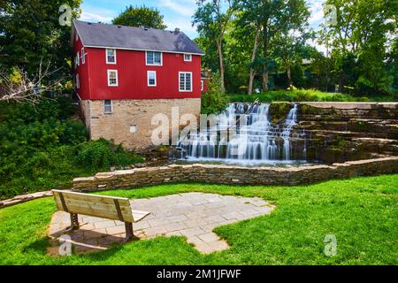 Rotes Haus am Fluss in der Stadt mit Wasserfall und Aussichtsplattform auf der Parkbank Stockfoto
