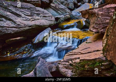 Aus nächster Nähe zu kleinem Wasserfall, umgeben von Flechten und Felsbrocken in weichem Licht Stockfoto