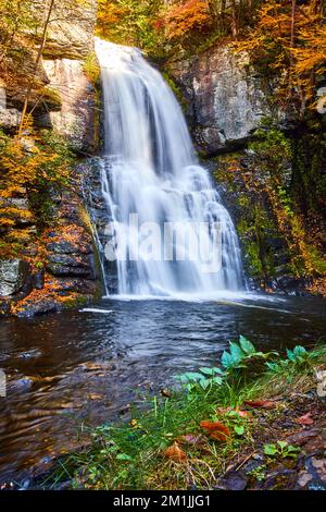 Ufer unter dem tosenden Wasserfall über Klippen mit gelben Blättern über den Felsen Stockfoto