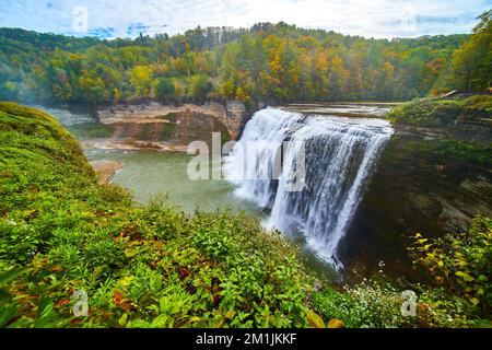 Riesiger Wasserfall aus nächster Nähe, der über Klippen in den Canyon in üppigem grünem Wald strömt, mit einem Hauch von herannahendem Fall Stockfoto