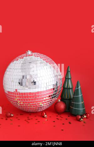 Disco-Ball mit Weihnachtsspielzeug auf rotem Hintergrund Stockfoto