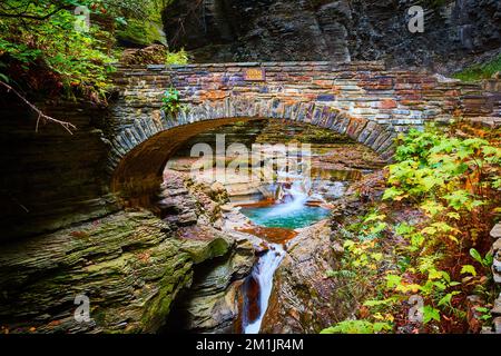 Wunderschöne Steinbogenbrücke über Schlucht und Fluss mit blauem Wasser und Wasserfällen im Herbst Stockfoto