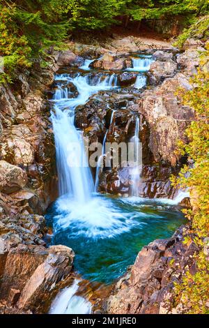 Wunderschöne blaue Wasserfälle, die sich in Eimer von Felsen mit Wald umschließen Stockfoto