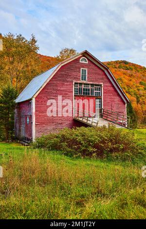 In der Nähe der wunderschönen roten Scheune, die auf Feldern mit bunten Herbstbergen altert Stockfoto