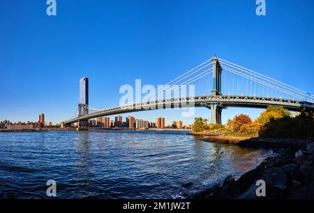 Panoramablick von Brooklyn auf die berühmte Manhattan Bridge über das blaue Wasser, das nach New York City mit blauem Himmel führt Stockfoto