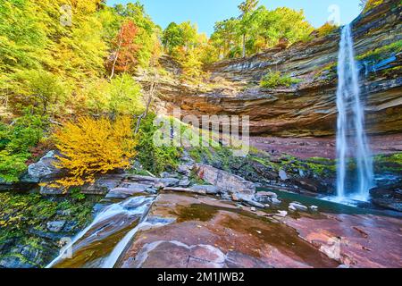 Mehrschichtige Klippen und Herbstlaub umgeben einen atemberaubenden großen Wasserfall über den Klippenrändern Stockfoto