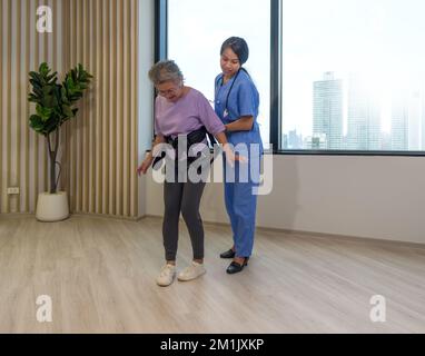 Eine Physiotherapeutin in blauer Uniform hilft älteren Menschen beim Sport und beim Gehen mit dem Sicherheitsgurt. Atmosphäre in Community Health CE Stockfoto