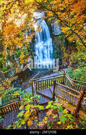 Treppen führen hinunter zu einem atemberaubenden großen Wasserfall über Klippen, umgeben von gelbem Herbstlaub Stockfoto