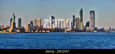Panoramablick bei Sonnenuntergang auf die Freiheitsstatue mit der Skyline von New Jersey Stockfoto
