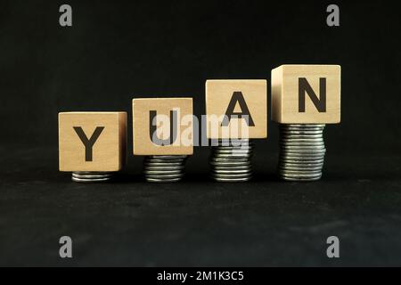 Das Konzept des wirtschaftlichen und finanziellen Wachstums und der Erholung der chinesischen Währung. Zunehmender Münzstapel auf dunkelschwarzem Hintergrund mit dem Wort "chinesischer Yuan". Stockfoto