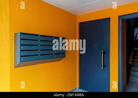 Graue Briefkästen an einer orangefarbenen Wand am Eingang eines Wohngebäudes Stockfoto