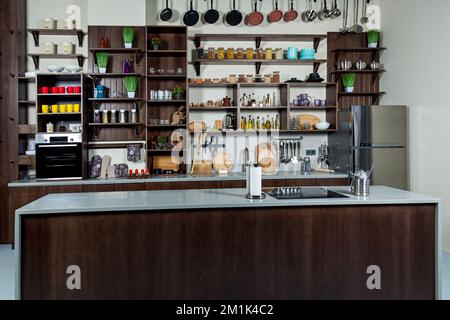 Arbeitsbereich der Küche. Küchenschrank mit Gläsern, Tassen, Gewürzen, Tellern, Küchenarbeitsfläche mit eingebautem Spülbecken, Herd und Standplatten Stockfoto