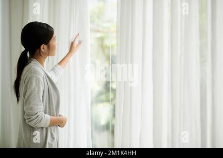 Junge Frau, die morgens Vorhänge öffnete Stockfoto