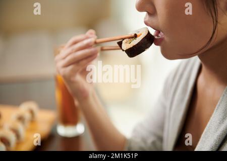Junge Frau, die köstliches Sushi im Restaurant isst Stockfoto
