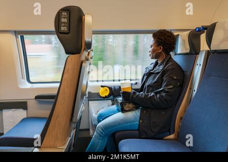 Eine Afrikanerin sitzt in einem Pendlerzug in Zentralschweden mit einer Tasse Kaffee in der Hand Stockfoto