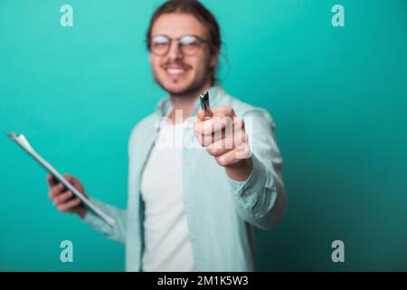 Glücklicher Geschäftsmann mit einer lächelnden Brille, der in Notizblock schreibt, mit Stift auf blauem Studiohintergrund. Weißer erfolgreicher junger Mann Stockfoto