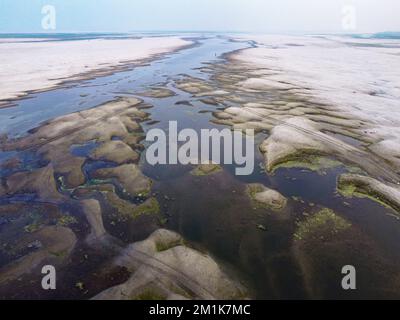 Bogura, Rajshahi, Bangladesch. 13.. Dezember 2022. Passagiere überqueren ein trockenes Flussbett zu Fuß in der Nähe des Jamuna River in Bogura, Bangladesch. Die meisten Wasserstraßen entlang des Jamuna-Beckens im Norden von Bangladesch sind bereits ausgetrocknet und haben riesige Sandbänke geschaffen, die die Boote und die Fahrgastbewegungen stören. Die Sandbänke, in Bengali als „chars“ bezeichnet, haben keine feste Position. Der Fluss legt sie in einem Jahr ab, sehr oft zur späteren Zerstörung, und legt sie in der nächsten Regenzeit wieder ab. Pendler müssen auf der Suche nach befahrbaren Zweigen des Flusses einen weiten Weg zurücklegen. Das sind sie Stockfoto