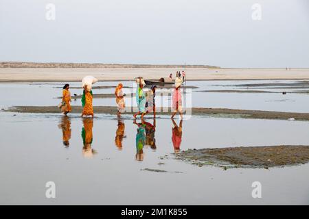 Bogura, Rajshahi, Bangladesch. 13.. Dezember 2022. Passagiere überqueren ein trockenes Flussbett zu Fuß in der Nähe des Jamuna River in Bogura, Bangladesch. Die meisten Wasserstraßen entlang des Jamuna-Beckens im Norden von Bangladesch sind bereits ausgetrocknet und haben riesige Sandbänke geschaffen, die die Boote und die Fahrgastbewegungen stören. Die Sandbänke, in Bengali als „chars“ bezeichnet, haben keine feste Position. Der Fluss legt sie in einem Jahr ab, sehr oft zur späteren Zerstörung, und legt sie in der nächsten Regenzeit wieder ab. Pendler müssen auf der Suche nach befahrbaren Zweigen des Flusses einen weiten Weg zurücklegen. Das sind sie Stockfoto