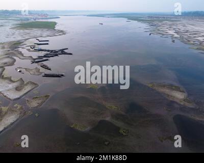 Bogura, Rajshahi, Bangladesch. 13.. Dezember 2022. Passagiere überqueren ein trockenes Flussbett zu Fuß in der Nähe des Jamuna River in Bogura, Bangladesch. Die meisten Wasserstraßen entlang des Jamuna-Beckens im Norden von Bangladesch sind bereits ausgetrocknet und haben riesige Sandbänke geschaffen, die die Boote und die Fahrgastbewegungen stören. Die Sandbänke, in Bengali als „chars“ bezeichnet, haben keine feste Position. Der Fluss legt sie in einem Jahr ab, sehr oft zur späteren Zerstörung, und legt sie in der nächsten Regenzeit wieder ab. Pendler müssen auf der Suche nach befahrbaren Zweigen des Flusses einen weiten Weg zurücklegen. Das sind sie Stockfoto