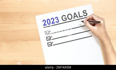 Die menschliche Hand, die die 2023-Zielliste schreibt, steht auf dem Zettel. Ziele für 2023. Frohes Neues Jahr 2023 Stockfoto