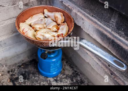 Spanische Mahlzeit im Freien. Frisch gebratene Hähnchenflügel auf einer Pfanne in einem Campinggasofen Stockfoto