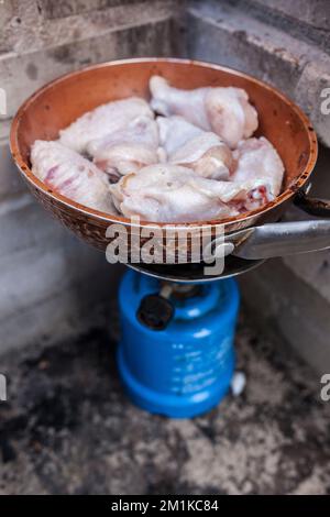 Spanische Mahlzeit im Freien. Frisch gebratene Hähnchenflügel auf einer Pfanne in einem Campinggasofen Stockfoto