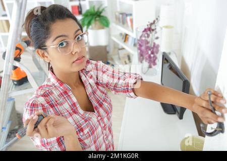 Junge, seriöse Frau, die zu Hause einen Bohrer für heimwerker benutzt Stockfoto