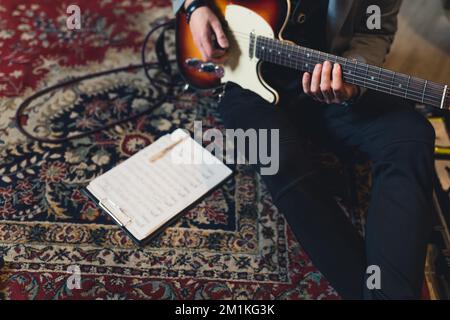 Gitarrist auf gemustertem Teppich mit elektrischer Gitarre und Notizzettel. Draufsicht. Nicht wiedererkennbare Person. Hochwertiges Foto Stockfoto