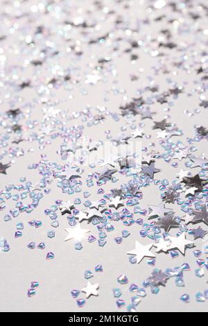 Leuchtende silberne Sterne und Konfetti aus Kristallen auf blauem Pastellhintergrund. Selektiver Fokus. Festliche Textur. Stockfoto