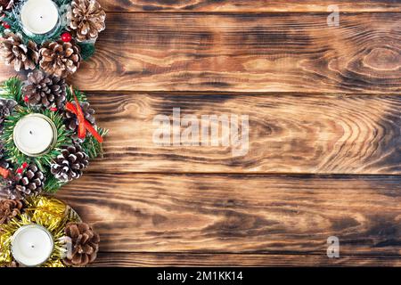 Weihnachtsdekorationen aus Kerzen und Kiefernzapfen, Schneeflocken, grünen Zweigen des Weihnachtsbaums auf einem Holztisch. Stockfoto