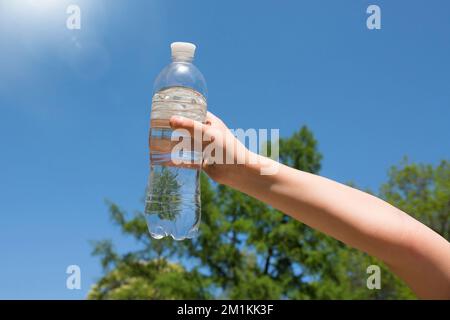 Die Hand eines Kindes hält eine Flasche Trinkwasser gegen den blauen Himmel Stockfoto