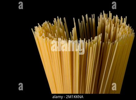 Gelbe lange Spaghetti auf schwarzem Hintergrund. Dünne Pasta in Reihen. Gelbe italienische Pasta. Lange Spaghetti. Rohe Spaghetti Bolognese. Rohe Spaghetti Stockfoto