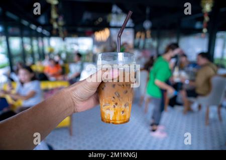 Halten Sie ein Kunststoffglas Eiskaffee mit Milch auf verschwommenem Hintergrund mit der Hand Stockfoto