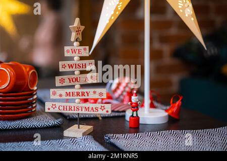 Wir wünschen Ihnen fröhliche Weihnachtsworte auf einem hölzernen Weihnachtsbaum dekorierten Weihnachtstisch zu Hause, bereiten uns auf das neue Jahr vor und packen Weihnachtsgeschenke ein. Stockfoto