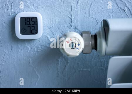 Heizkörper mit Temperaturregler. Ein Thermometer, das Grad und Feuchtigkeit in der Wohnung anzeigt. Wintergasheizung. Stockfoto