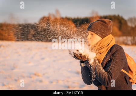 Eine Frau bläst eine Handvoll Schnee bei Sonnenuntergang aus ihren Händen Stockfoto