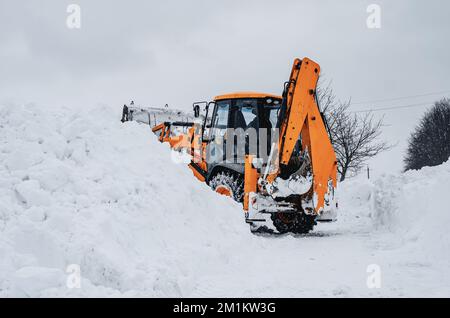 Der große gelbe Traktor reinigt Schnee von der Straße. Reinigung und Reinigung von Straßen in der Stadt von Schnee im Winter Stockfoto