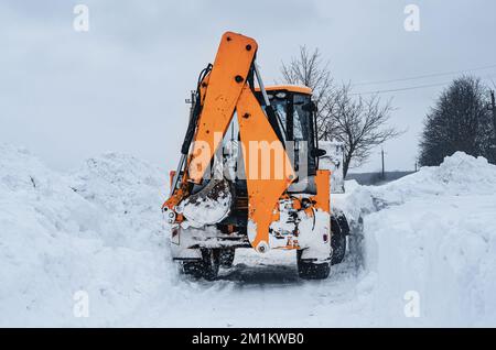 Der große gelbe Traktor reinigt Schnee von der Straße. Reinigung und Reinigung von Straßen in der Stadt von Schnee im Winter Stockfoto