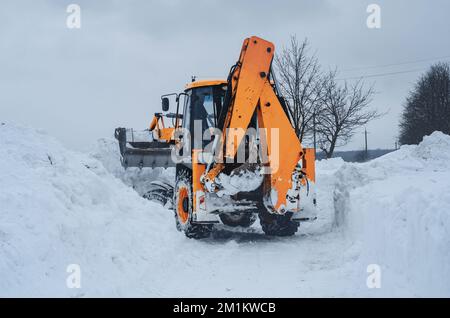 Der große gelbe Traktor reinigt Schnee von der Straße. Reinigung und Reinigung von Straßen in der Stadt von Schnee im Winter Stockfoto
