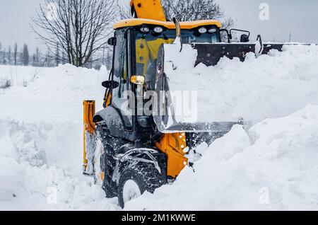 Der große gelbe Traktor reinigt Schnee von der Straße. Reinigung und Reinigung von Straßen in der Stadt von Schnee im Winter Stockfoto
