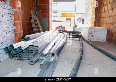 A few black long hoses for plastering walls under pressure, heap of thermal insulation material Styrofoam and pile of new galvanized, metal profiles f Stockfoto