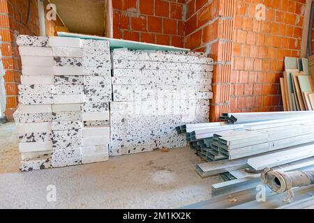 Heap of thermal insulation material Styrofoam and pile of new galvanized, metal profiles for drywalls arranged on the floor waiting to be installed. Stockfoto