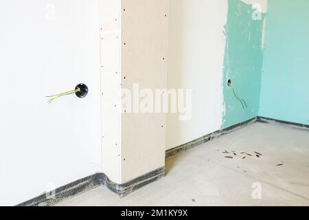 Freiliegende Steckdose mit entfernter oberer Abdeckung für die Installation der Verkabelung an der Putzwand des im Bau befindlichen Gebäudes. Stockfoto