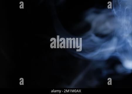 Anmutige Wirbel aus blauem Rauch auf schwarzem Hintergrund. Nahaufnahme von Dampf. Weichzeichner und Textur von Helios 44m-4-Objektiv im Vintage-Design. Abstrakter Hintergrund. Stockfoto