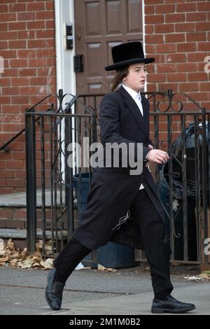 Ein orthodoxer jüdischer junger Mann mit langer Peyot- und schwarzer Kleidung läuft zügig am nördlichen Ende der Lee Avenue in Brooklyn, New York City. Stockfoto