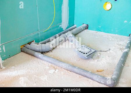 Wasserinstallation im neuen unfertigen Badezimmer, freiliegende graue PVC-Abwasserrohre, die an der Stelle für eine Duschkabine montiert sind. Stockfoto