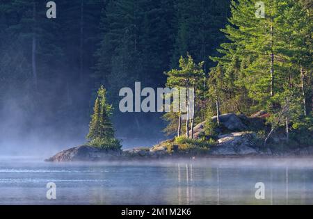 Ein gemütliches Landschaftsbild, das aufgenommen wird, wenn die Sonne an einem felsigen Punkt am Wolf Lake in Temagami, Ontario, aufgeht. Stockfoto