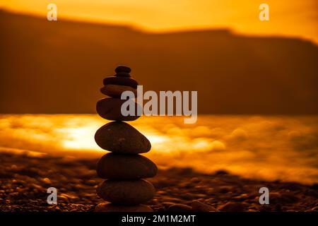 Kieselpyramiden-Silhouette am Strand. Sonnenuntergang mit Meer im Hintergrund. Zen Stones on the Sea Beach Konzept, Ruhe, Gleichgewicht. Selektiver Fokus Stockfoto