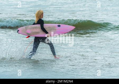 Eine eifrige junge Surferin, die ihr farbenfrohes Surfbrett im Fistral Beach in Newquay in Cornwall in England trägt. Stockfoto